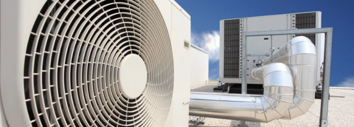 Close-up of rooftop HVAC system with large condenser fan and metal ductwork against a blue sky.